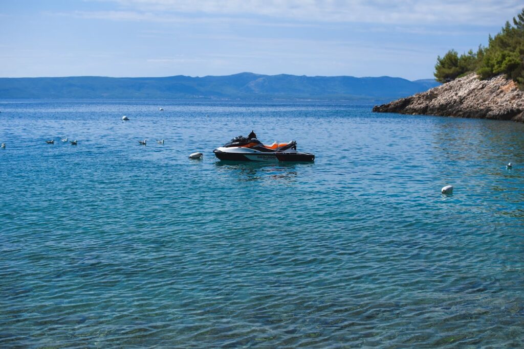 Relaxing coastal view of a jet ski on calm blue waters near a rocky coastline.